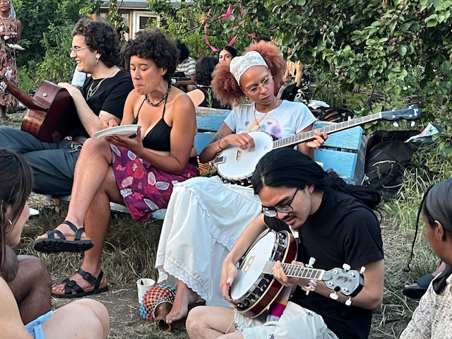 Several people of colour learning the banjo at an outdoors social gathering