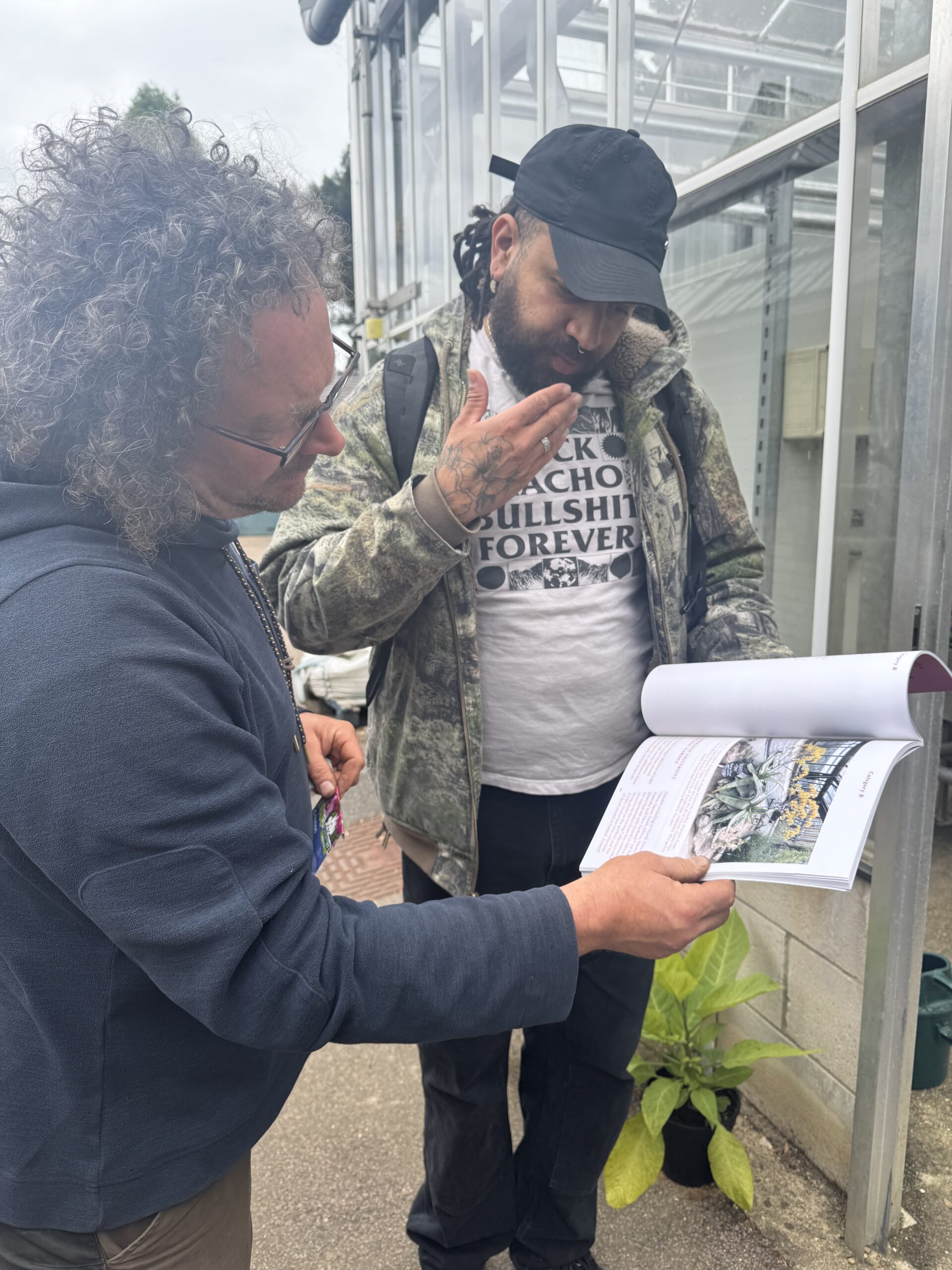 Two men examining a horticultural catalogue outside by a greenhouse