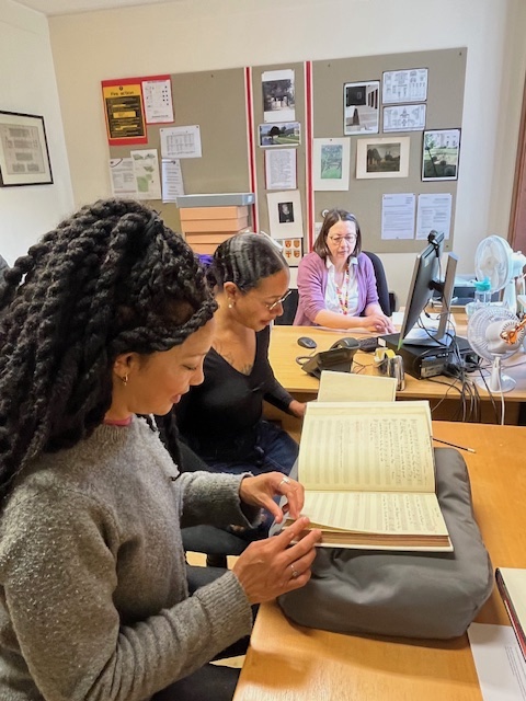 Three people consulting notebooks in an archive