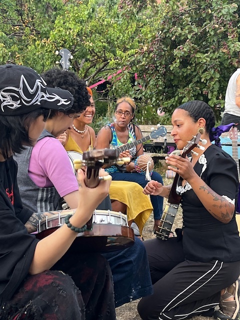 People of colour playing banjo at an outdoor social gathering