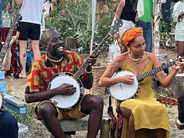 Two people of colour learning the banjo at an outdoors social gathering